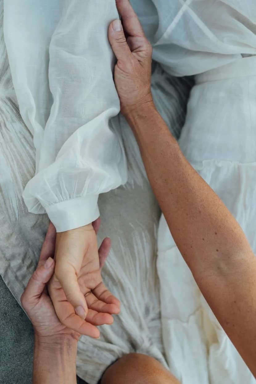 Close-up of a hand resting on a client's wrist during a body psychotherapy session, in white linen