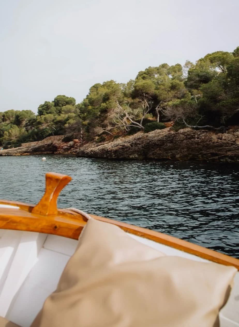 View from a wooden boat of a quiet, tree-lined cove near Cal Reiet, Mallorca
