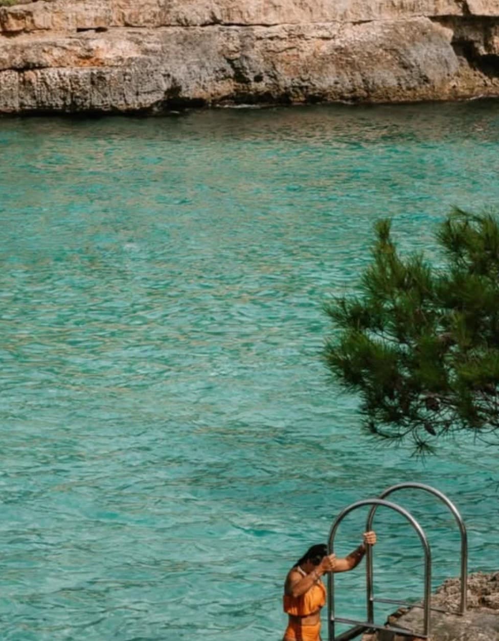 A person climbing a ladder into the turquoise water of a cove near Santanyí, Mallorca