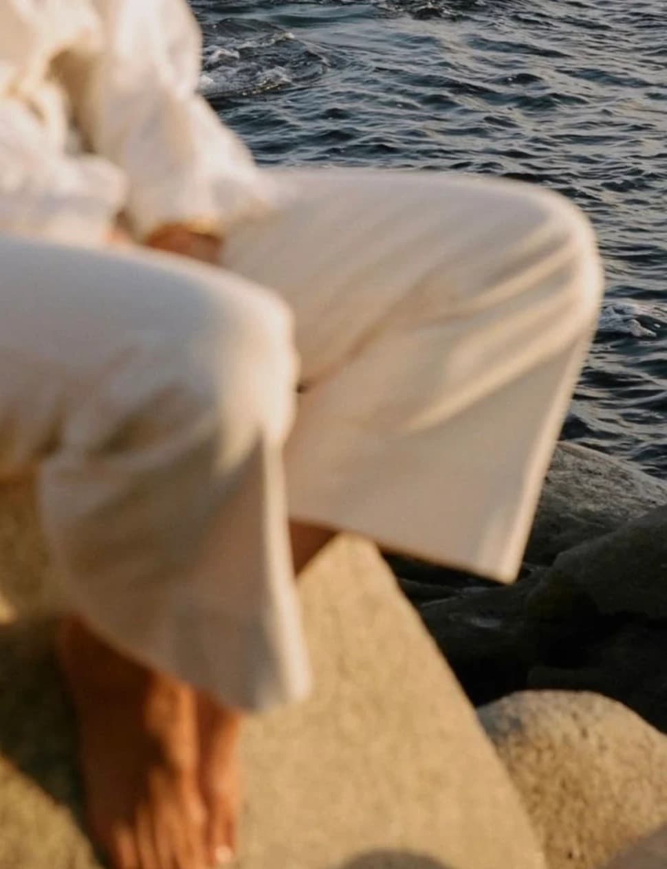 Two people in white clothing sitting quietly on rocks by the sea