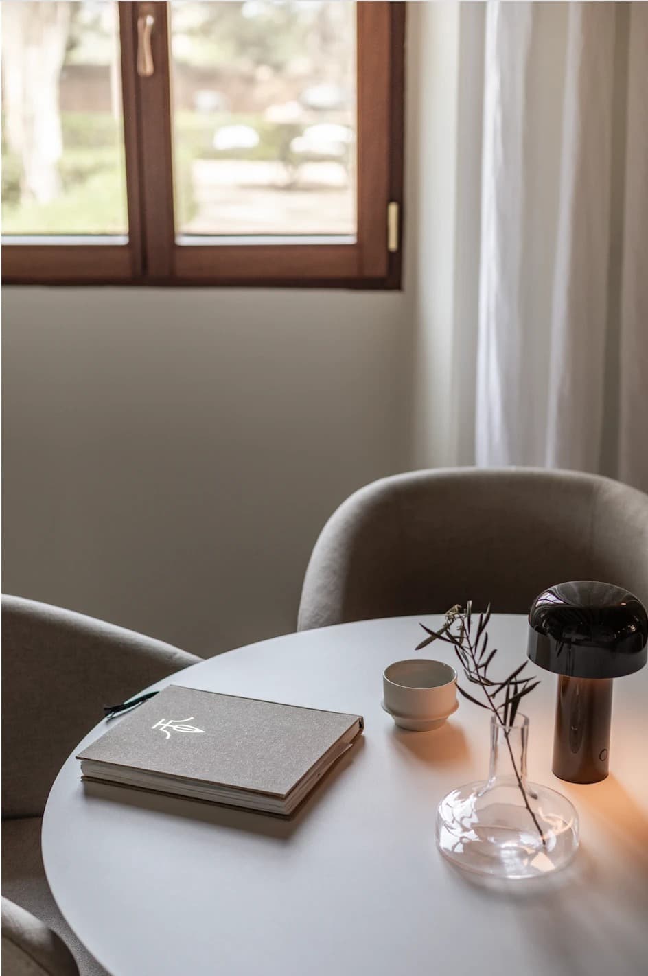 A round table detail at Cal Reiet with a notebook, teacup, olive branch and lamp