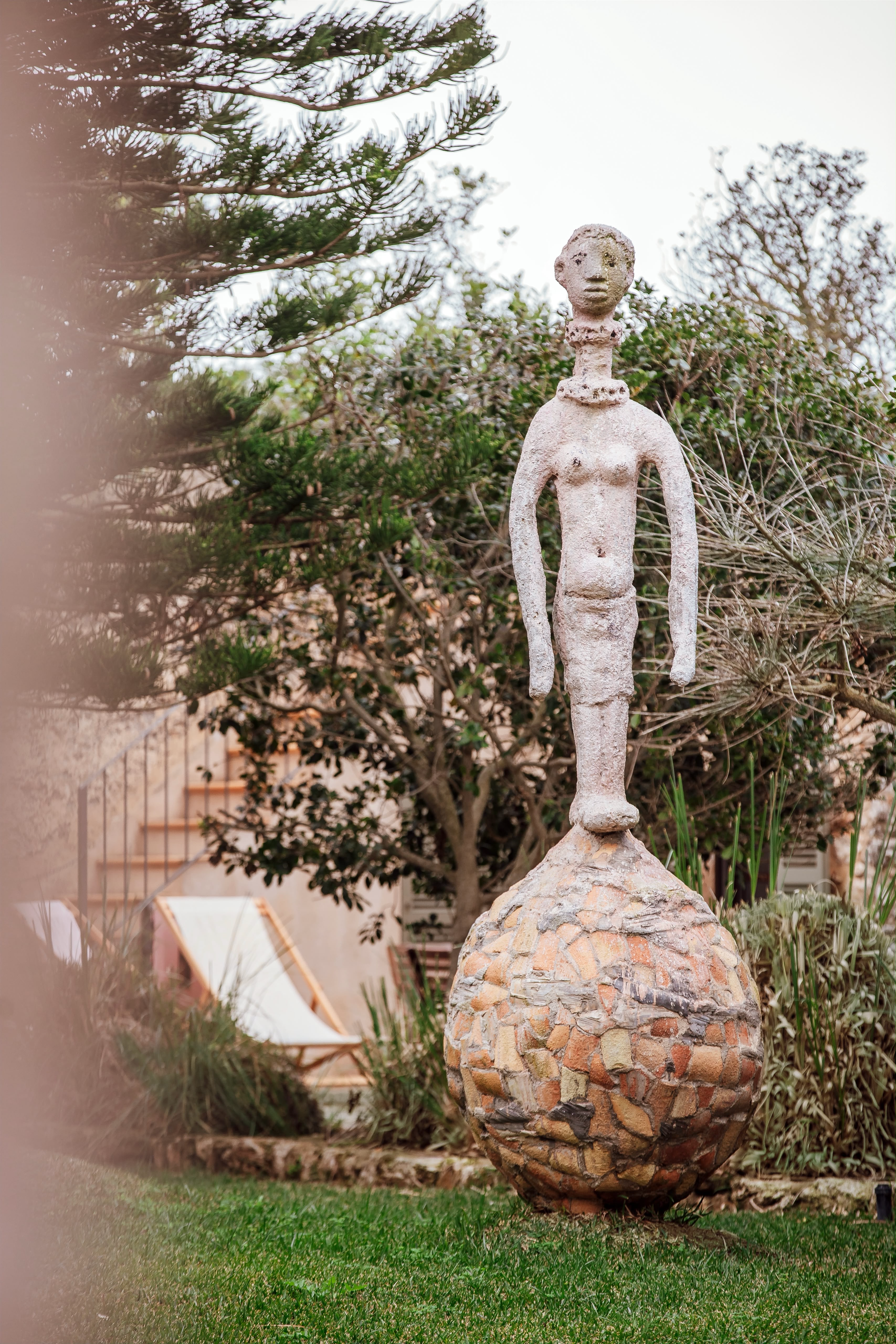 Slender sculpture of a figure balancing on a mosaic sphere in the gardens of Cal Reiet