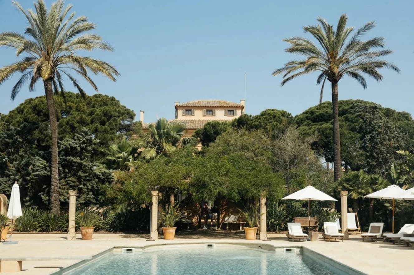 Ground-level view of the Cal Reiet pool framed by palm trees, with the main house behind