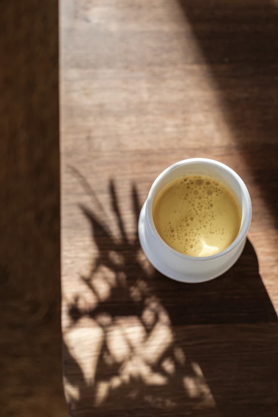 A cup of golden milk on a wooden table, dappled in leaf-shadowed sunlight
