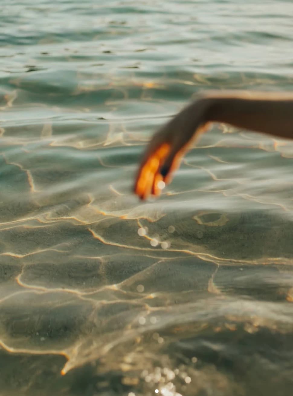 Close-up of a hand touching the surface of the sea, sunlit ripples around it